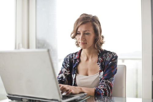 Eine Frau sitzt an einem Tisch und arbeitet am Laptop