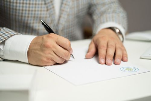 Ein Mann sitzt am Schreibtisch und schreibt auf ein Blatt Papier.