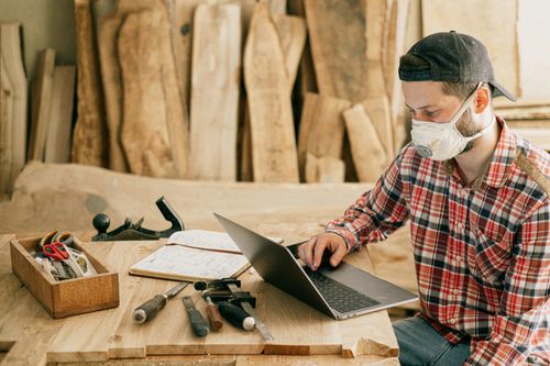 Ein Handwerker sitzt mit einer Staubschutzmaske vor seinem Laptop und schreibt eine Rechnung